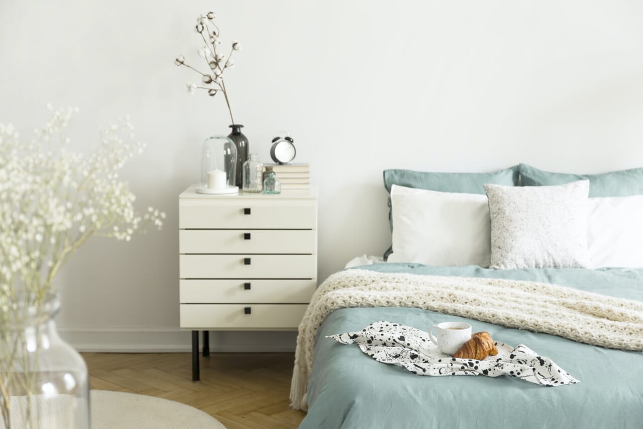A bright bedroom interior with sage green and white bedding, pil A bright bedroom interior with sage green and white bedding, pil
